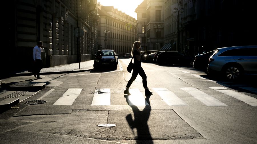 Backlit image of a woman crossing a pedestrian crosswalk.