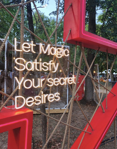 Neon sign in English within a red frame. It says Let's magic satisfy your secret desires