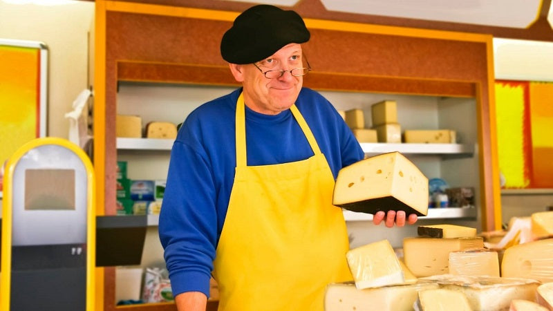 Man cheese seller in a store shows a piece of the product.