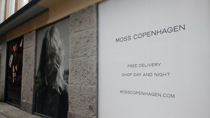 Facade of the Moss store showing a shop window, a large photograph of a blonde woman's face, and a wall with the Moss brand.