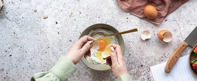 Overhead image of a woman's hands cracking an egg into a bowl of flour.