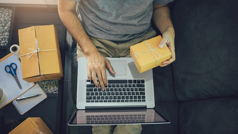Man at his computer holding a package in his hand.