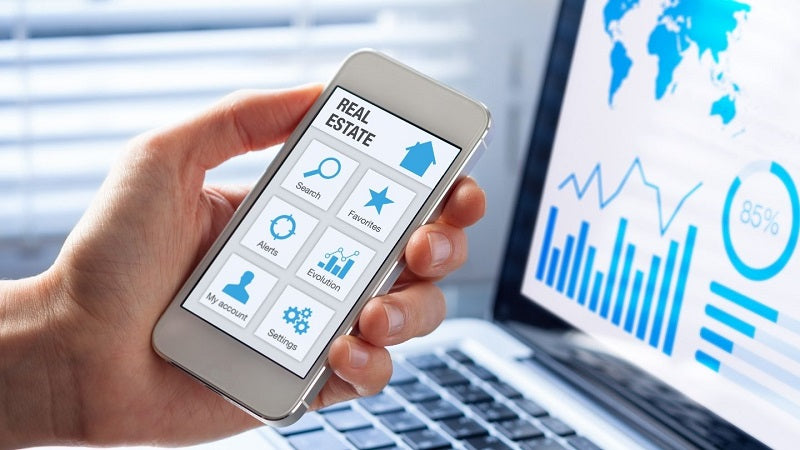 Graphs on a computer screen and a hand holding a mobile phone showing an app.