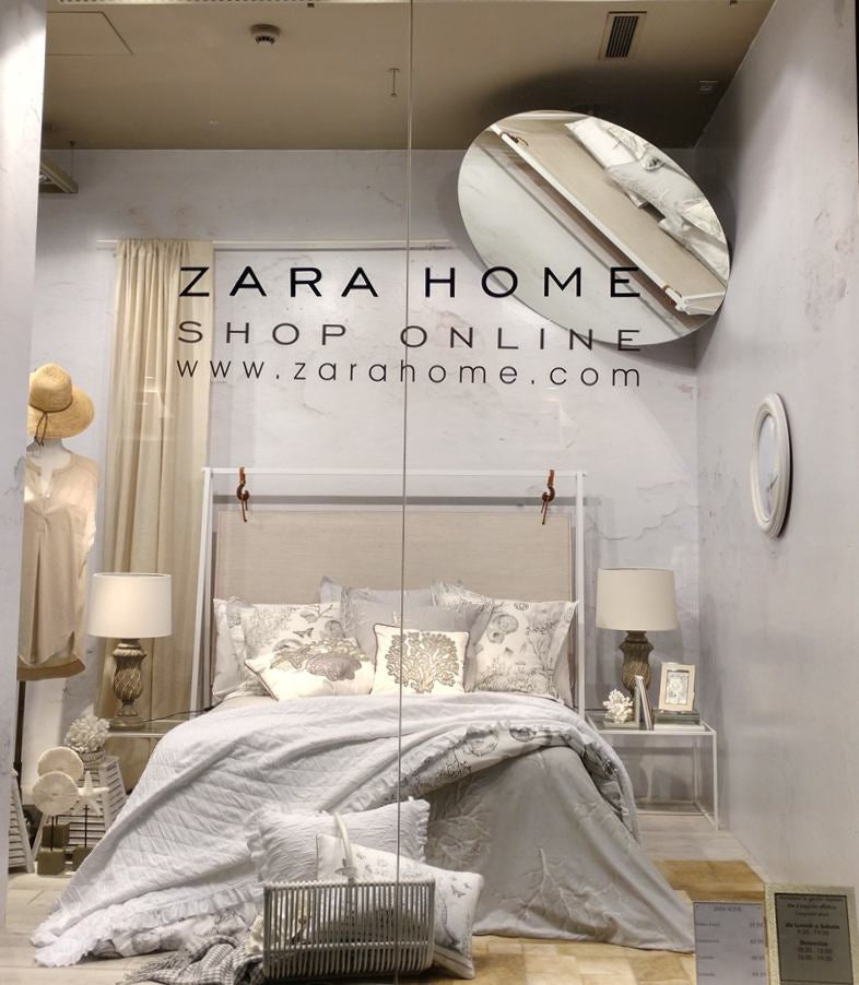 Shop window showing a bed with gray-toned bedding and cushions, from the Zara Home brand
